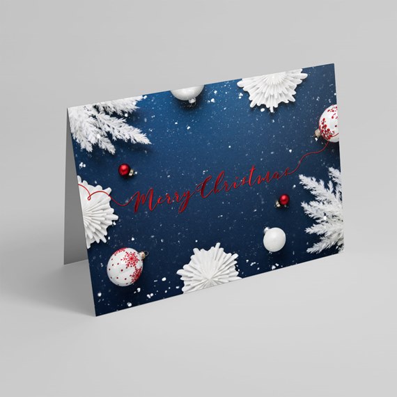 Folded holiday greeting card with navy background, white snowflake and frosted foliage accents, red and white ornaments, and red cursive 