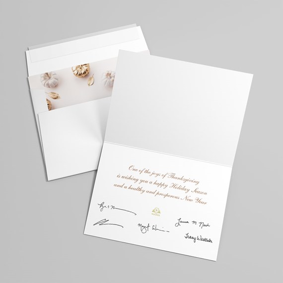 white folded holiday greeting card with gold script message, signatures and an envelope lined with beige and gold pumpkin motif