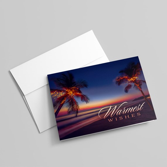Folded greeting card and white envelope showing a sunset beach with lit palm trees and the words 