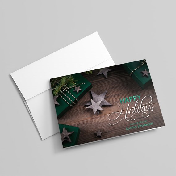 Folded holiday greeting card with wood background, green gift boxes and star decorations on a white envelope.