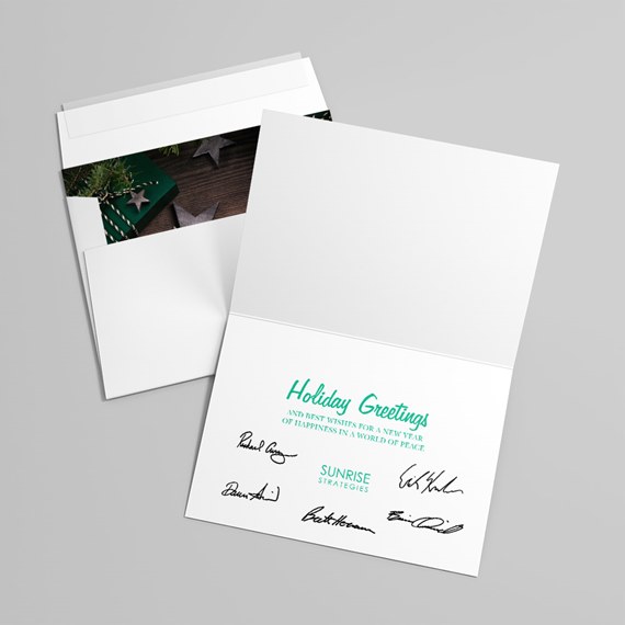 Open folded holiday greeting card with teal "Holiday Greetings" text, printed message and signatures, plus matching envelope with green liner