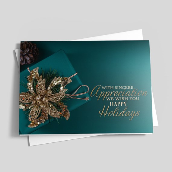 Holiday greeting card with teal background, gold glitter poinsettia decoration, greenery and gold script text, with white envelope