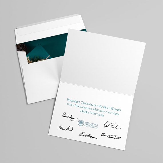 Open white holiday greeting card with teal printed message and black signatures beside a white envelope with dark teal lining