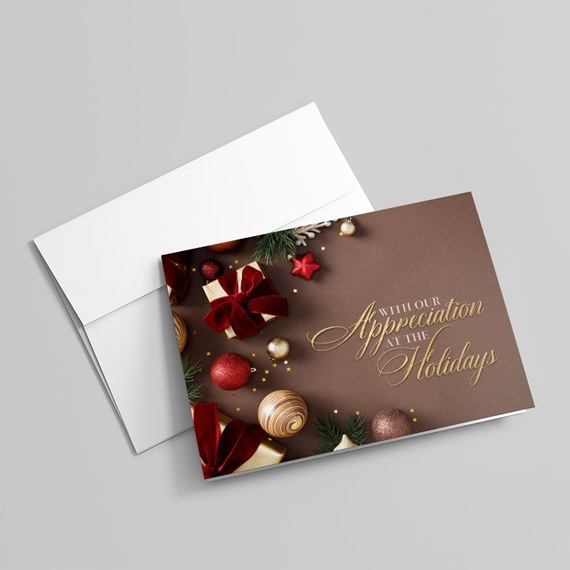 Holiday greeting card with brown background, gold lettering, red bows and ornaments and pine accents next to a white envelope