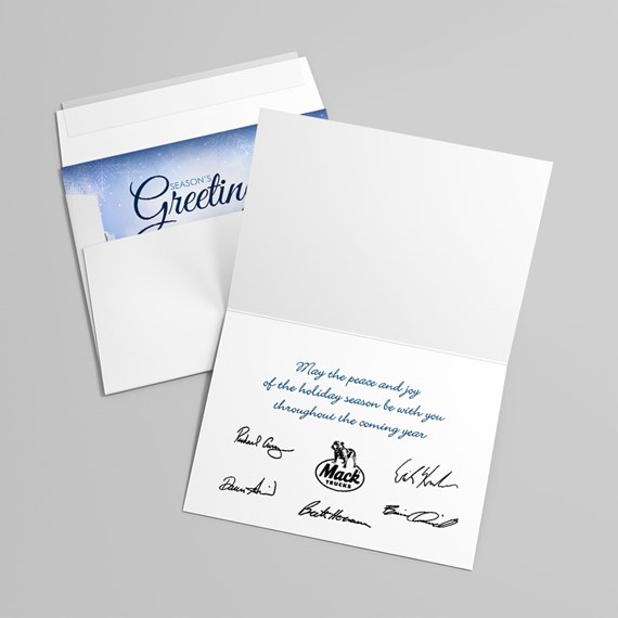 Folded white holiday greeting card with blue cursive message and printed signatures, shown with matching envelope and blue seasonal liner