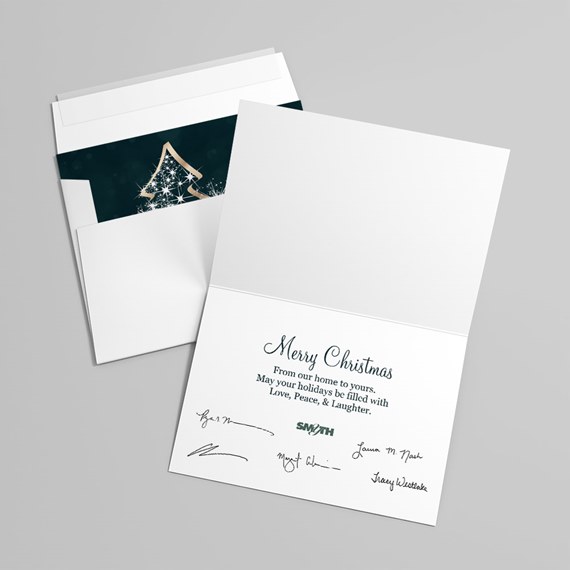 Folded white Christmas greeting card with printed message and signatures, paired with envelope revealing dark green insert with gold tree