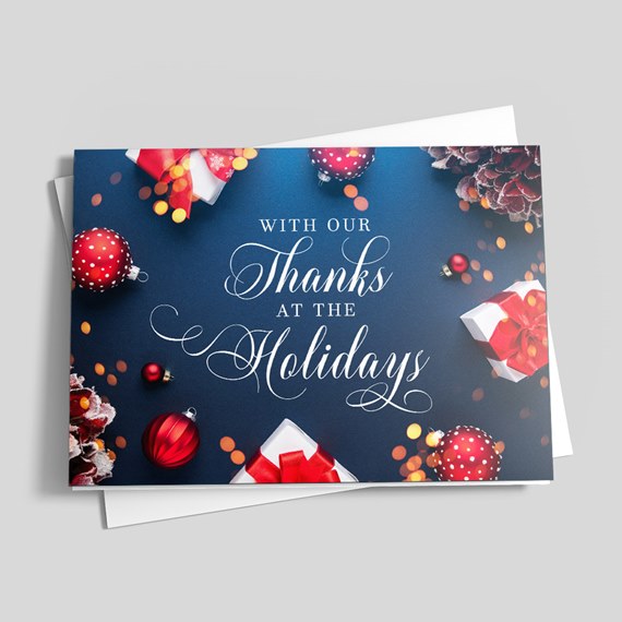 Folded holiday thank-you card with navy background, white script text, red ornaments and wrapped gifts