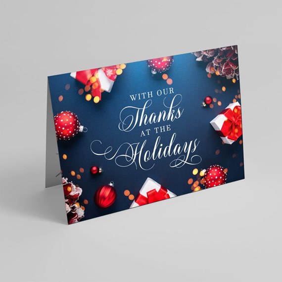 Folded holiday thank-you card with navy background, white script text, red ornaments and wrapped gifts