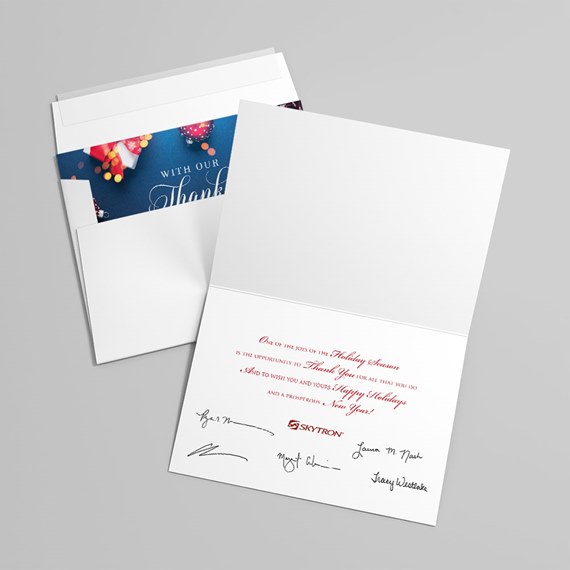 open white folded greeting card with red printed holiday message, signature lines, and envelope showing a blue decorative insert